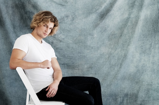 Retrato da moda de jovem em poses de camisa branca em estúdio sobre fundo azul