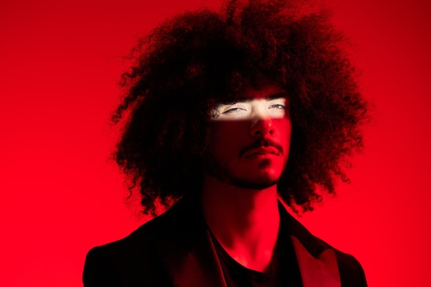 Retrato da moda de um homem com cabelo encaracolado em um conceito moderno de tendência multinacional de luz colorida de fundo vermelho