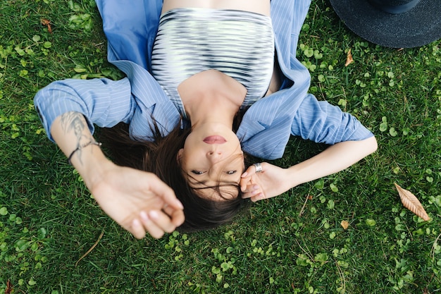 Retrato da moda de uma jovem vestida com uma jaqueta azul listrada. mulher deitada em um gramado verde em um parque na cidade