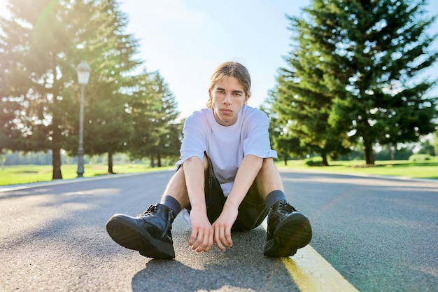 Retrato da moda do rapaz adolescente hipster sentado na estrada