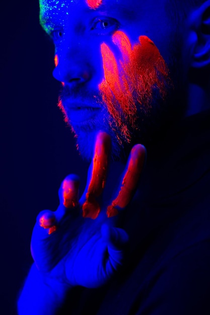 Retrato da moda Um homem com tinta fluorescente no rosto sob luz neon