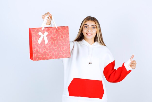 Retrato da modelo de uma bela mulher em pé com uma sacola de presente e mostrando o polegar