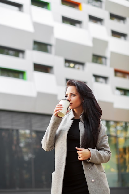 Retrato da mulher de negócio da autoconfiança com café a ir ao lado do escritório.