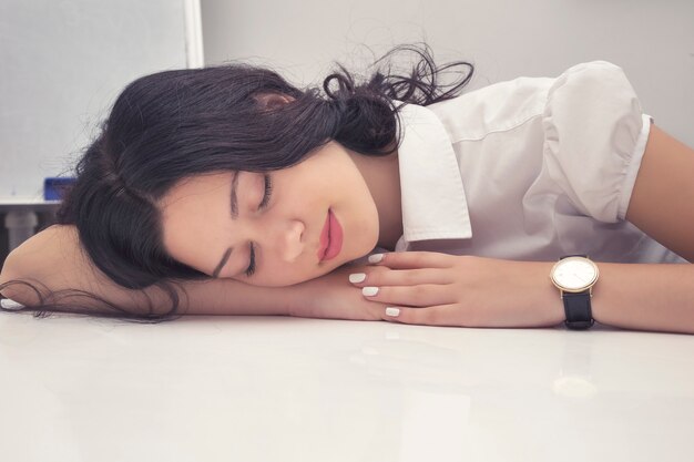 Retrato da mulher de negócios nova inquieta que sente a falta de sono e que dorme na mesa do trabalho.