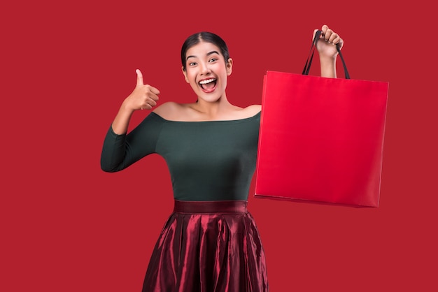 Retrato da mulher feliz nova feliz que levanta com os sacos de compras sobre o fundo vermelho.