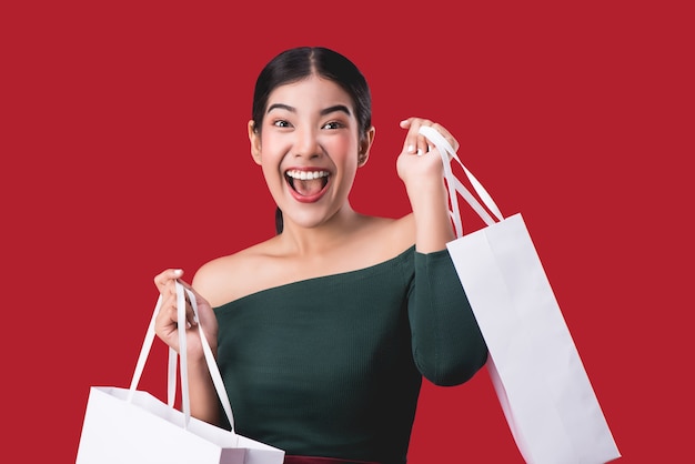 Retrato da mulher feliz nova feliz que levanta com os sacos de compras sobre o fundo vermelho.
