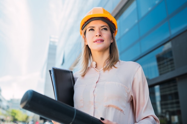 Retrato da mulher profissional do arquiteto que veste o capacete amarelo e que está ao ar livre. Conceito de engenheiro e arquiteto.