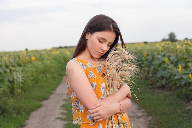 Retrato da natureza O close de uma linda mulher vestida está mantendo a colheita de trigo em suas mãos enquanto está no campo de trigo amarelo