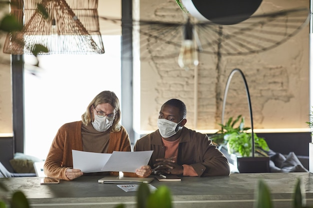 Retrato da vista frontal de dois homens colaborando no projeto durante a reunião de negócios e usando máscaras no escritório ou no interior do café, copie o espaço