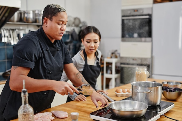 Retrato da vista lateral da chef feminina fritando carne durante a aula de culinária no interior da cozinha