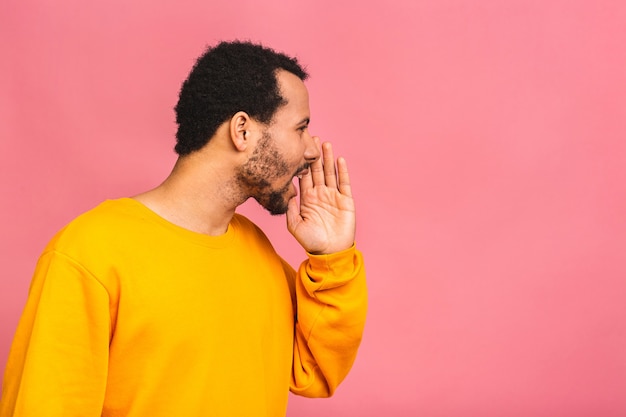 Foto retrato da vista lateral de um jovem gritando em voz alta com a mão na boca isolada em rosa.