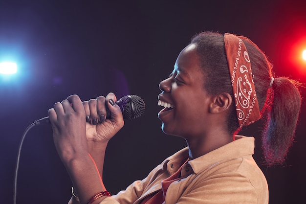 Retrato da vista lateral de uma jovem afro-americana cantando ao microfone enquanto está no palco