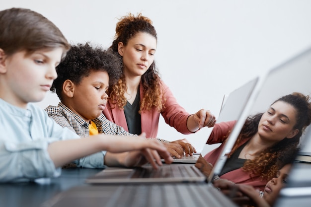 Foto retrato da vista lateral de uma jovem professora ajudando um menino usando o laptop durante a aula de ti na escola