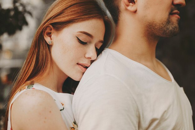 Retrato da vista lateral de uma linda mulher ruiva com sardas, abraçando o namorado por trás com os olhos fechados, enquanto namorava do lado de fora.