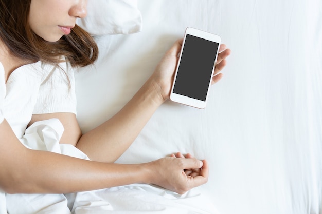 Retrato da vista superior de uma mulher viajante cansada dormindo na cama com o celular na mão