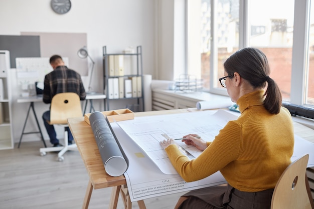 Retrato da vista traseira da arquiteta desenhando plantas enquanto está sentado à mesa no escritório,