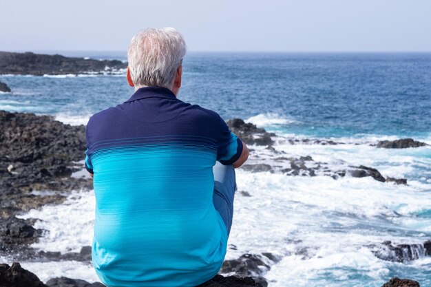 Foto retrato da vista traseira de um homem sênior sozinho vestindo camiseta azul, desfrutando de liberdade ao ar livre e férias no mar homem de cabelos brancos idoso durante a aposentadoria, olhando para o horizonte sobre a água