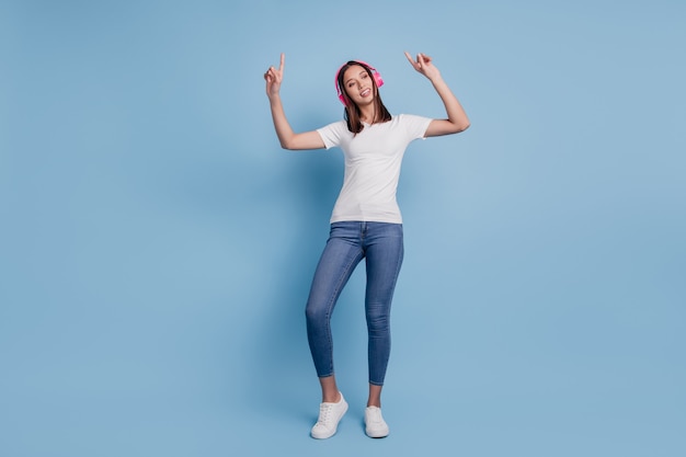 Retrato de dama agradable soñadora despreocupada llevar auriculares bailar escuchar música sobre fondo azul.