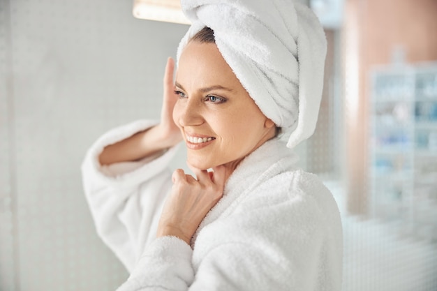 Retrato de una dama alegre con el pelo envuelto en una toalla de baño mirando a otro lado