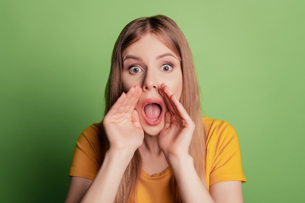 Retrato de dama divertida sorprendida con la boca abierta decirle a secreto usar camiseta amarilla aislada sobre fondo de color verde