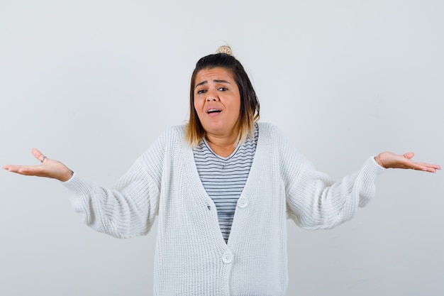 Retrato de dama encantadora mostrando gesto de impotencia en camiseta, chaqueta de punto y mirando confundido