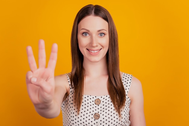 Retrato de dama encantadora positiva contar dedos muestran tres sobre fondo amarillo