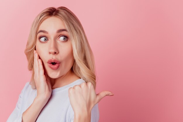 Retrato de dama interesada indica pulgar espacio vacío boca abierta cara impresionado sobre fondo rosa