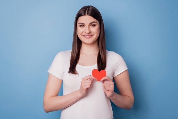 Retrato de dama linda cariñosa mantenga poco papel tarjeta roja en forma de corazón sobre fondo azul.