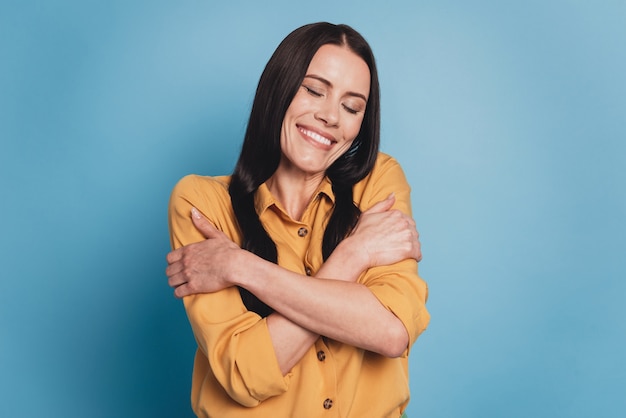 Foto retrato de dama positiva alegre abrazar los hombros cerrar los ojos sobre fondo azul.