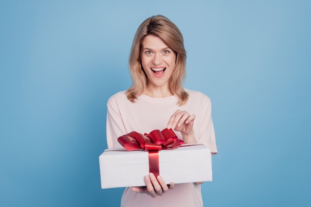 Retrato de dama sorprendida sorprendida emocionada mantenga caja de regalo boca abierta reacción omg sobre fondo azul.