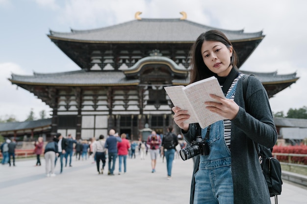 retrato de una dama taiwanesa leyendo una guía de fondo borroso templo todaiji. una mujer asiática que sostiene un manual está aprendiendo sobre la historia del famoso edificio religioso.