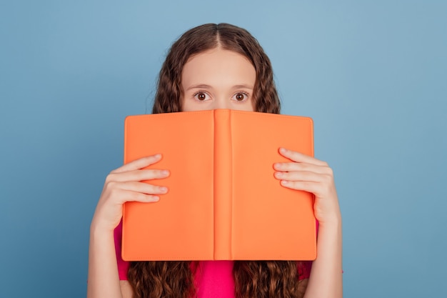 Retrato de dama tímida mantenga la mitad de la cara de la portada del libro mirar la cámara sobre fondo azul.