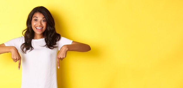 Foto retrato de adolescente africana-americana feliz mostrando banner apontando dedos para baixo no espaço da cópia