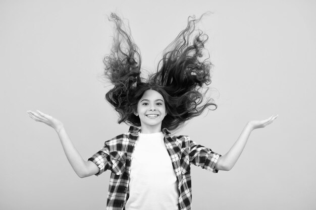 Retrato de adolescente com cabelo de movimento louco Jovem adolescente com cabelo fluído Adolescente morena com cabelo a voar em movimento Isolado em amarelo Adolescente feliz emoções positivas e sorridente de adolescente