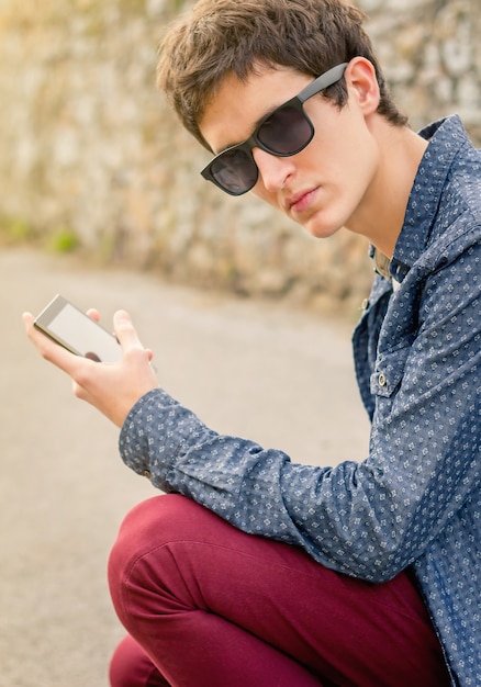 Retrato de adolescente hippie com óculos de sol usando seu telefone inteligente ao ar livre