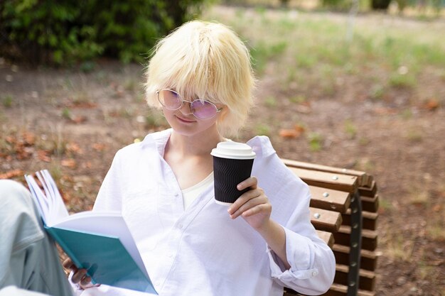 Retrato de adolescente lendo livro com bebida em copo de papel