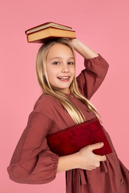 Retrato de adolescente segurando livros na cabeça e sorrindo
