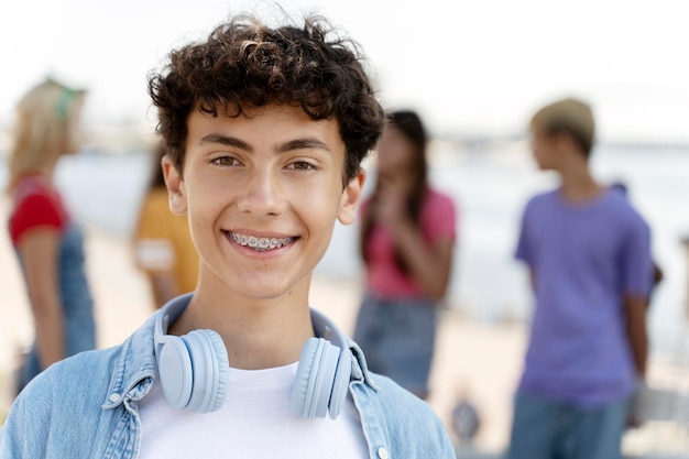 Retrato de adolescente sorridente com aparelho ortopédico usando fones de ouvido olhando para a câmera de pé na rua
