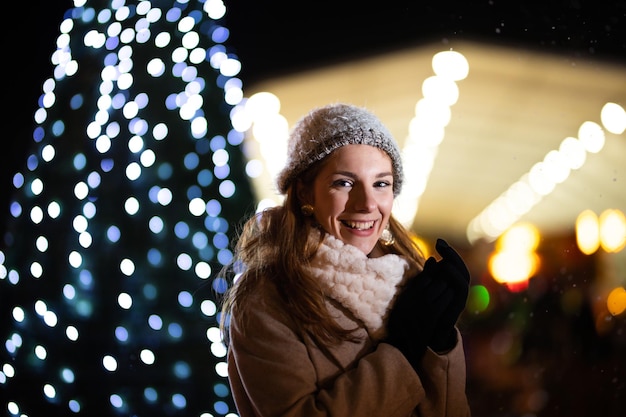 Retrato de adolescente sorridente, vestindo roupas de inverno ao ar livre. Árvore de Natal ao fundo.