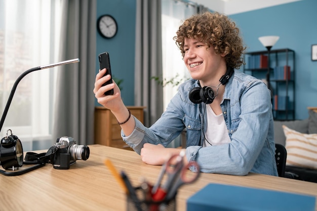 Retrato de adolescente usando telefone inteligente e sorrindo na mesa na sala de estar em casa homem segurando e nós