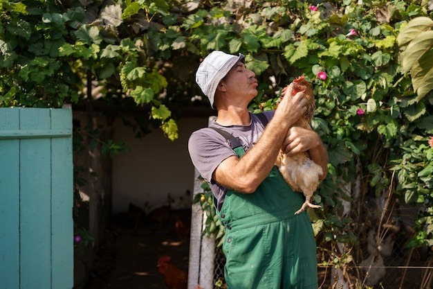 Foto retrato de agricultor caucasiano feliz segurando uma galinha marrom ao ar livre homem maduro sorridente com frango na mão com espaço de cópia