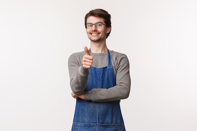 Retrato de alegre jovem satisfeito no avental, mostrar polegar para cima e sorrindo, garantir que você vai gostar de café em sua loja, aprovar ótimo lugar sair e desfrutar de sobremesas,