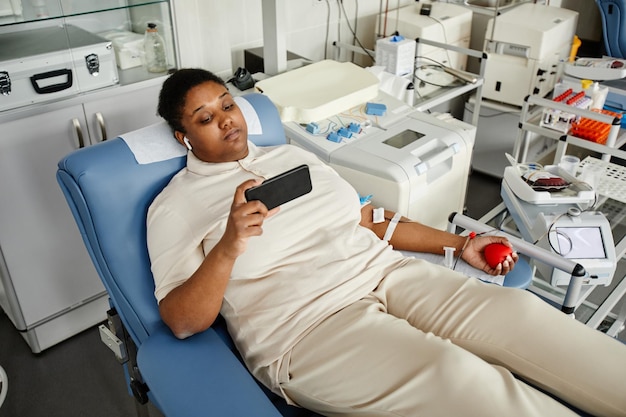 Retrato de alto ângulo de mulher negra dando sangue enquanto estava deitado na cadeira no centro de doação de sangue e h