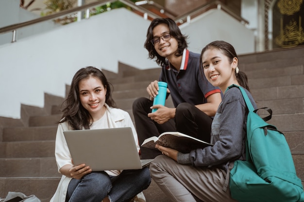 Retrato de alunos sentados trabalhando em grupos, olhando para a câmera na escada do campus