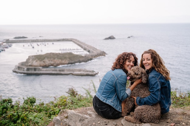 Retrato de amante do cão de mulheres, abraçando o cão de água marrom. Visão horizontal de mulheres viajando com animal de estimação. Estilo de vida com animais ao ar livre.