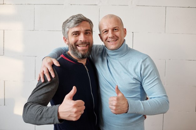 Retrato de amigos de meia-idade animados e positivos se abraçando e mostrando o polegar