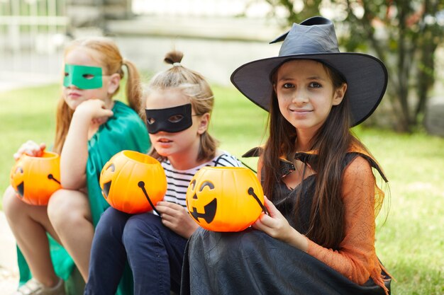 Retrato de amigos felizes em fantasias com abóboras sorrindo para a câmera ao ar livre na festa de halloween