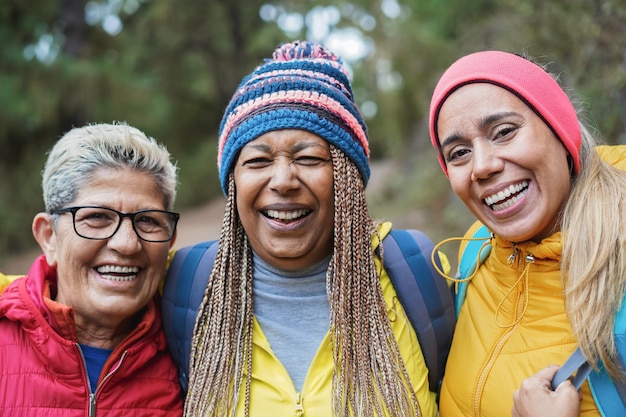 Retrato de amigos multirraciais sênior se divertindo durante o dia de caminhada na floresta - foco no rosto da mulher certa