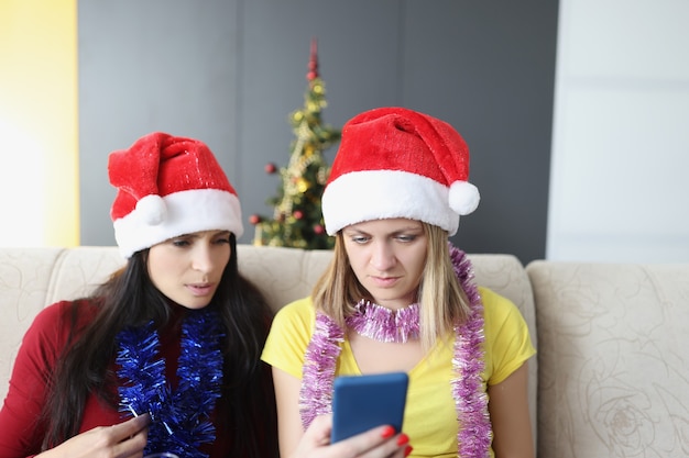 Retrato de amigos tentam se acostumar com o novo modelo de celular, descubra como se conectar à internet. Irmãs no sofá tentam chamar a família no ano novo. Celebração, tecnologia, conceito de natal