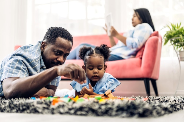 Retrato de amor feliz família negra pai e mãe afro-americanos com atividade sorridente de garotinha aprender e treinar habilidade do cérebro jogar com brinquedo construir blocos de madeira jogo de educação em casa